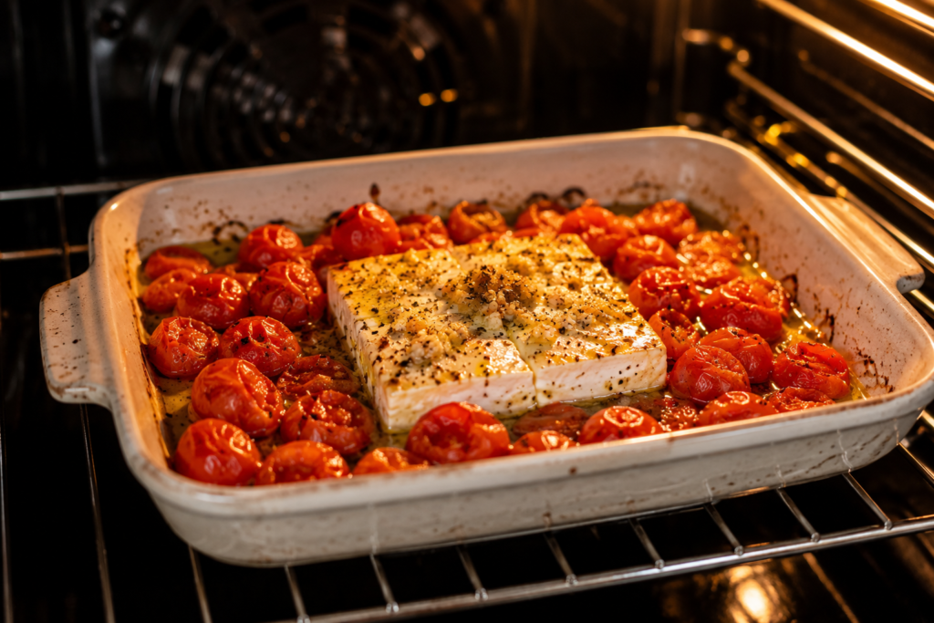 Feta cheese and cherry tomatoes roasting in a baking dish inside the oven for homemade baked feta pasta