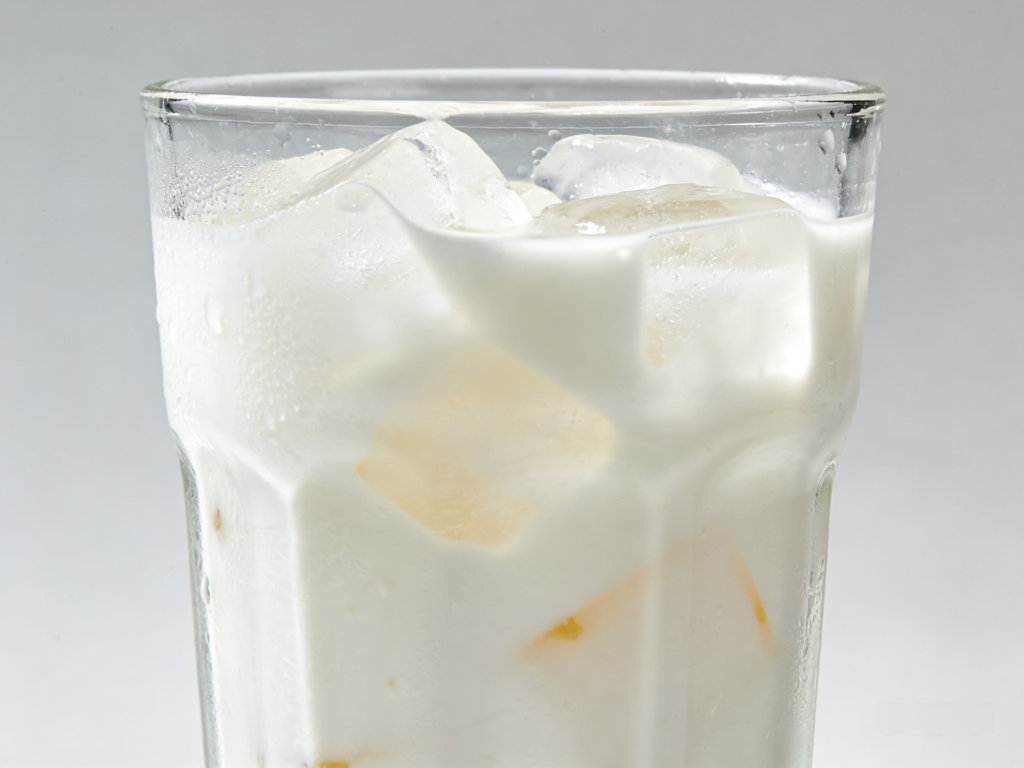 Tall glass filled with fresh white milk and ice cubes, ready for making dalgona coffee, refreshing drink base