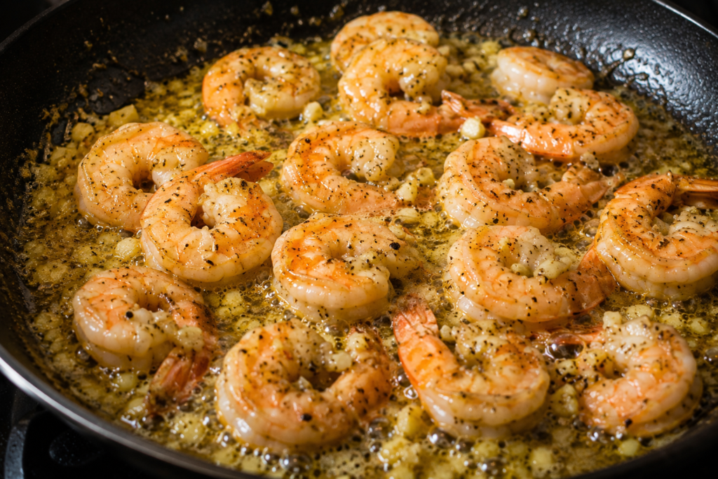 Shrimp cooking in rich garlic butter sauce inside a skillet, turning pink and juicy.