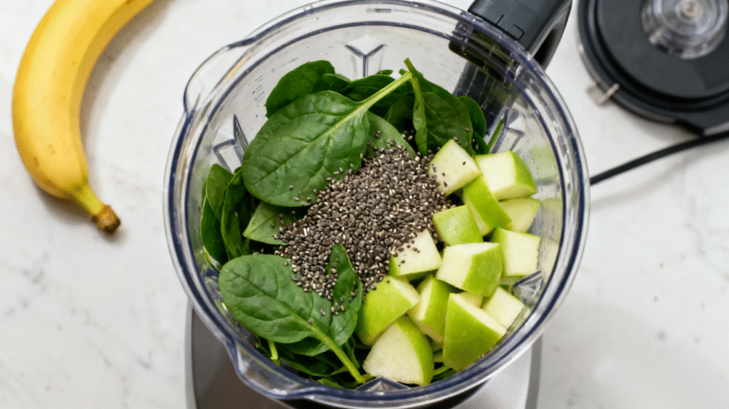 Banana, green apple, spinach, and chia seeds placed inside a blender for a homemade detox smoothie