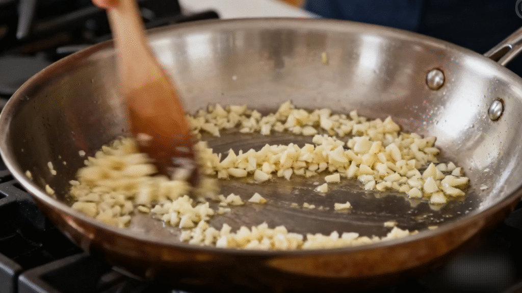 Garlic being stirred into sautéed vegetables to build rich flavor for pasta fagioli soup