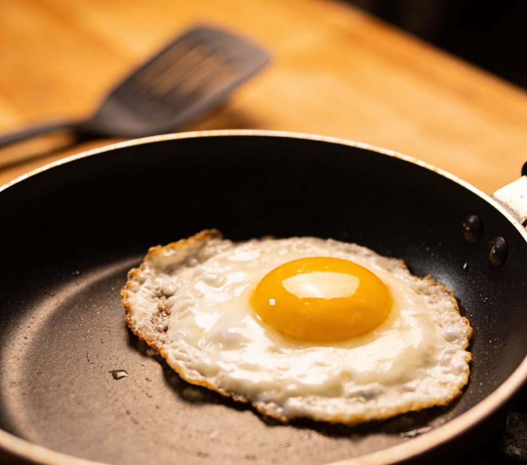 Fresh sunny side up eggs frying in a non-stick pan, hot oil, runny yolk, realistic cooking scene, home kitchen